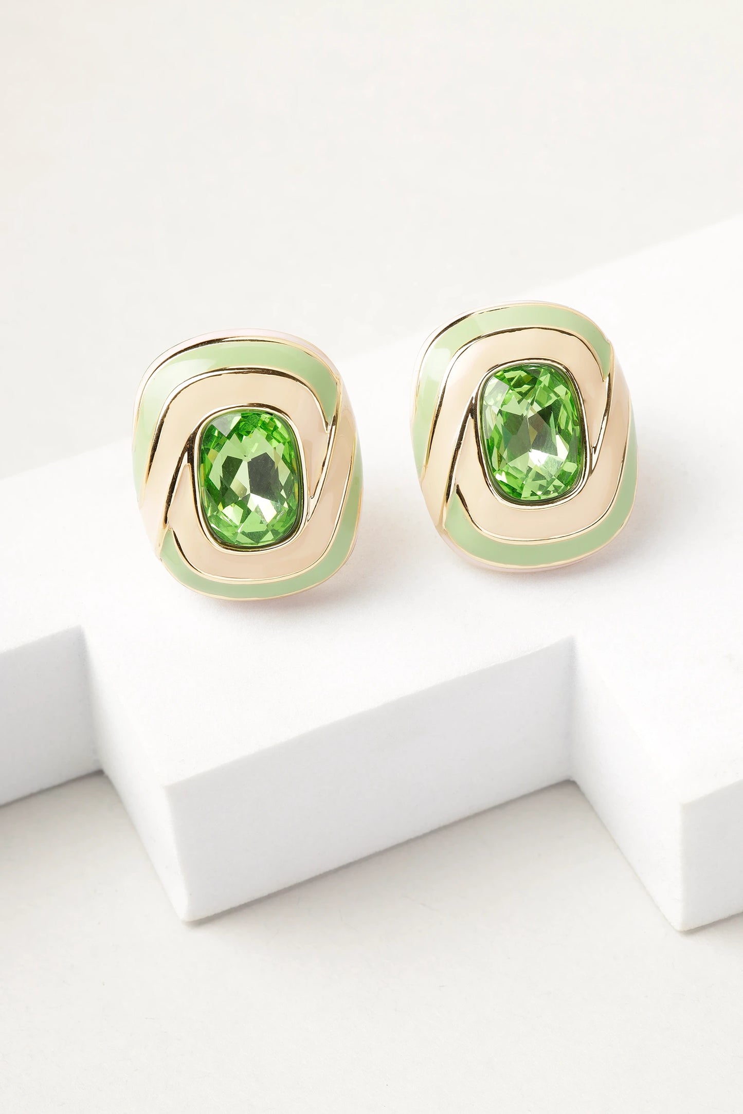 erde swirl stud earrings with green crystal and gold enamel detailing on white background
