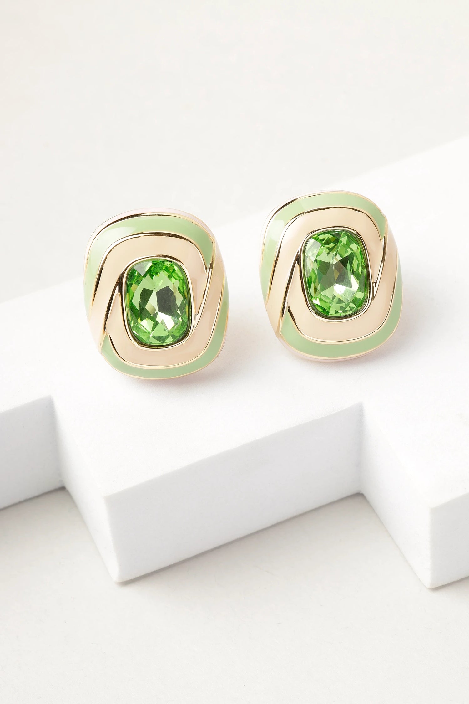 erde swirl stud earrings with green crystal and gold enamel detailing on white background