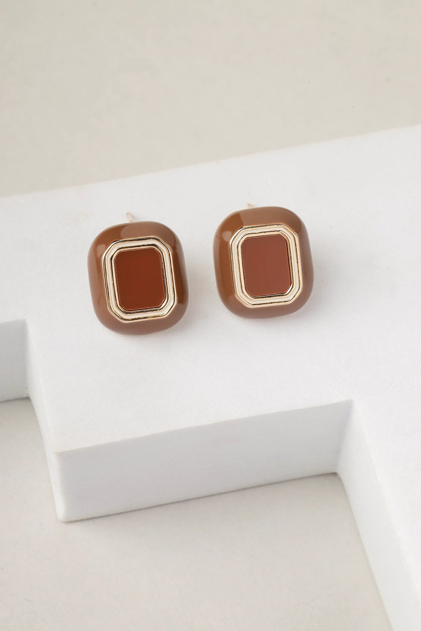 Close-up view of brown enamel gold stud earrings with geometric design