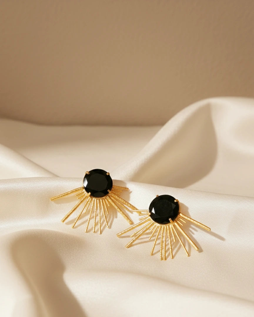 Black onyx gold sunburst statement earrings flat lay on fabric