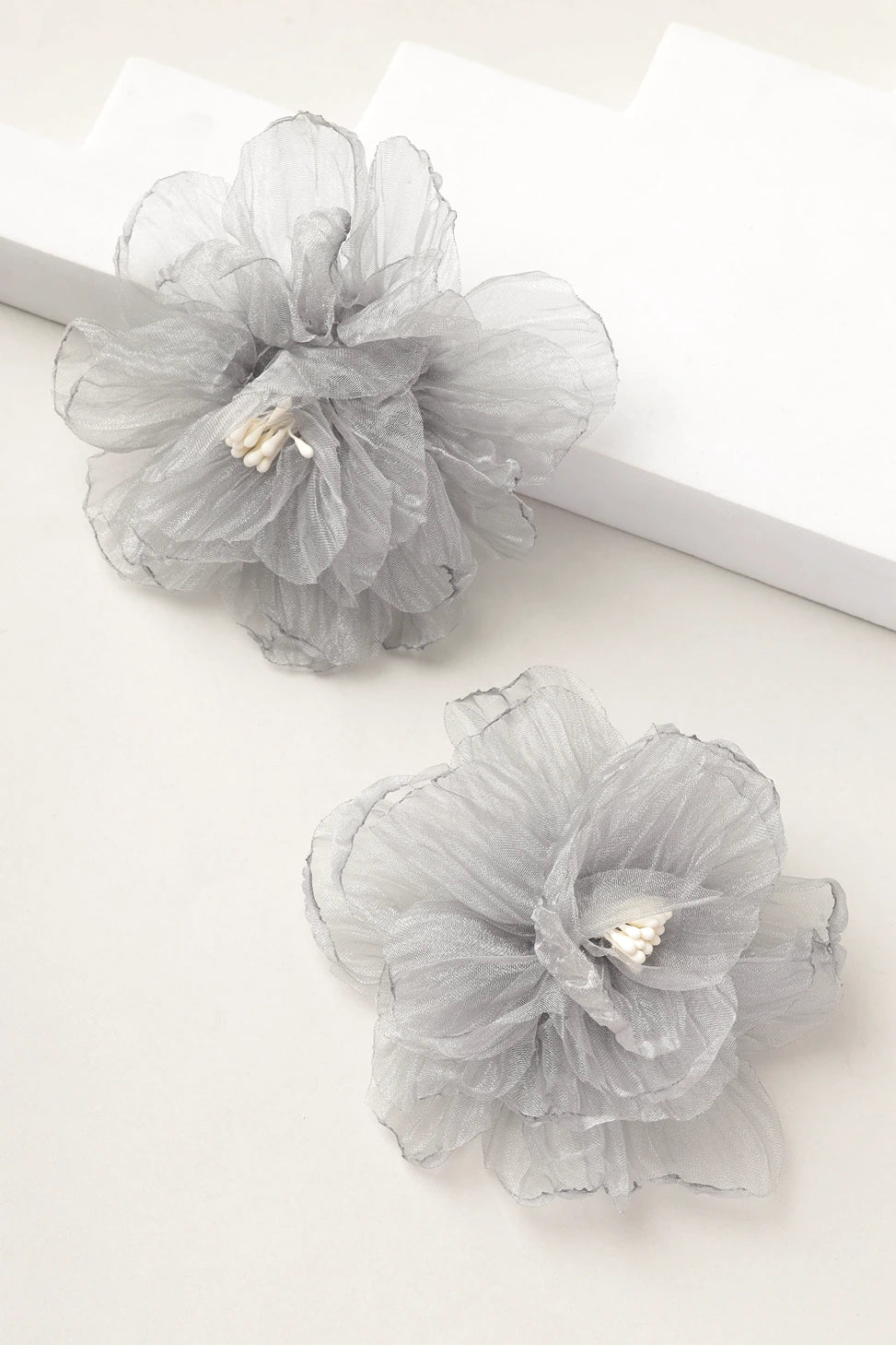 Styled shot of silver mist grey organza floral earrings on white blocks